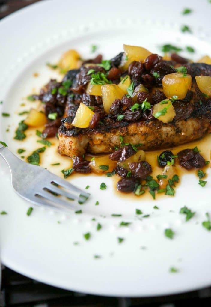 A close up of a boneless pork chop on a plate with apple raisin chutney.