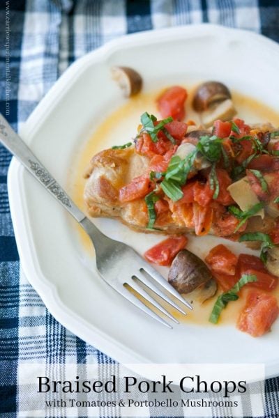 Braised boneless center cut pork chops with fire roasted tomatoes and Portobello mushrooms on a plate.