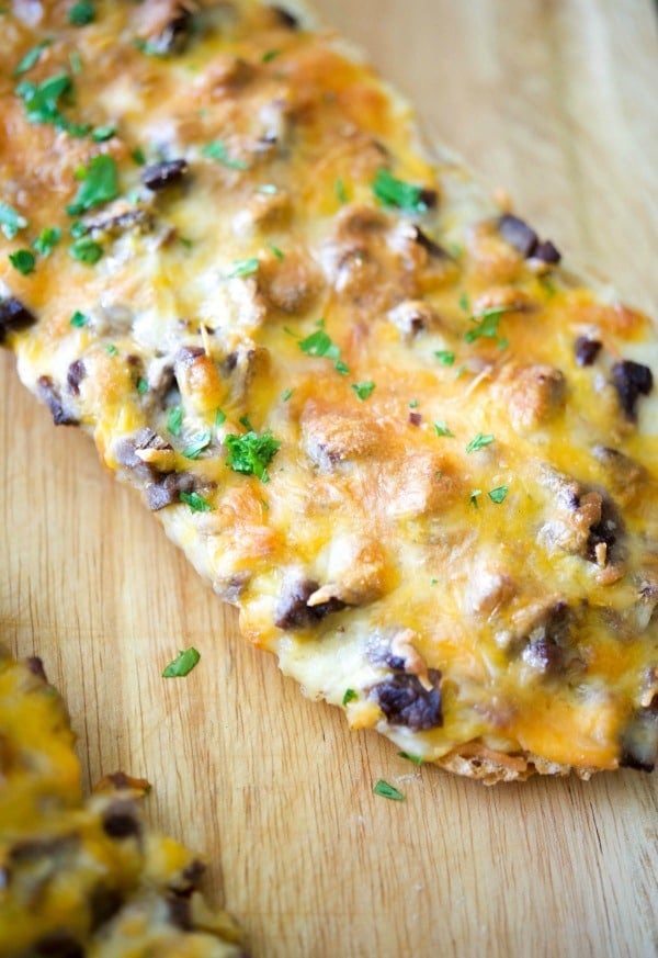 a close up of steak and cheddar french bread pizza on a board