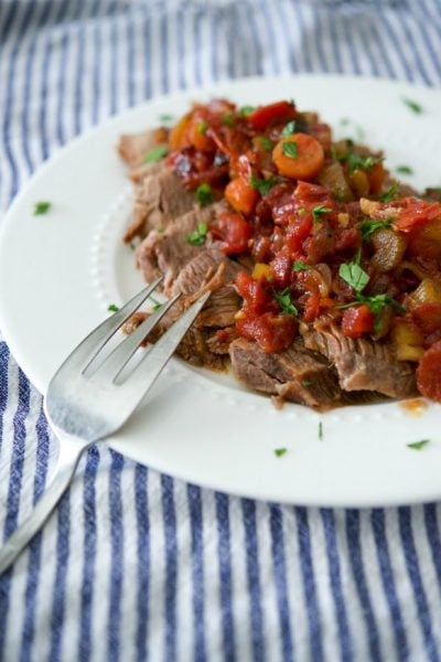A plate of food with a fork, with beef brisket and tomatoes.