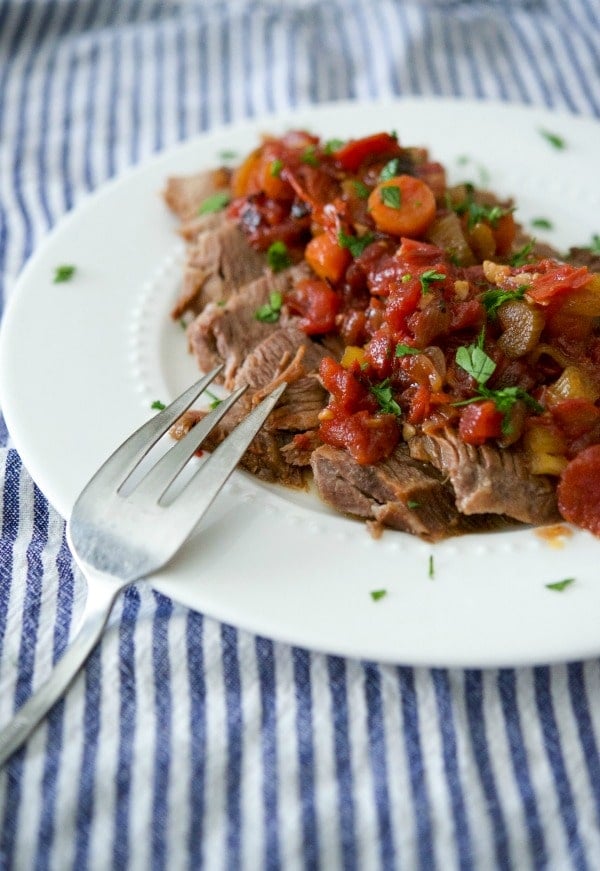 A plate of food with a fork, with beef brisket and tomatoes. 