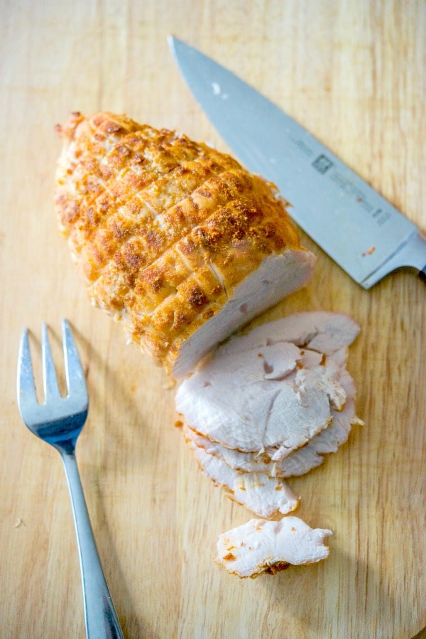 Boneless turkey breast seasoned with rotisserie seasonings on a wooden cutting board. 