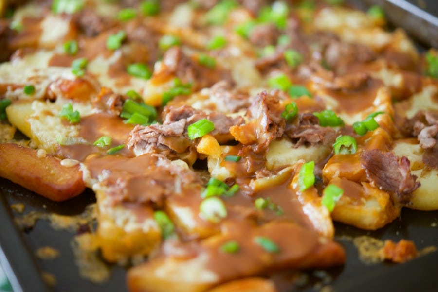 A close up of french fries on a sheet pan topped with gravy, cheese and roast beef. 