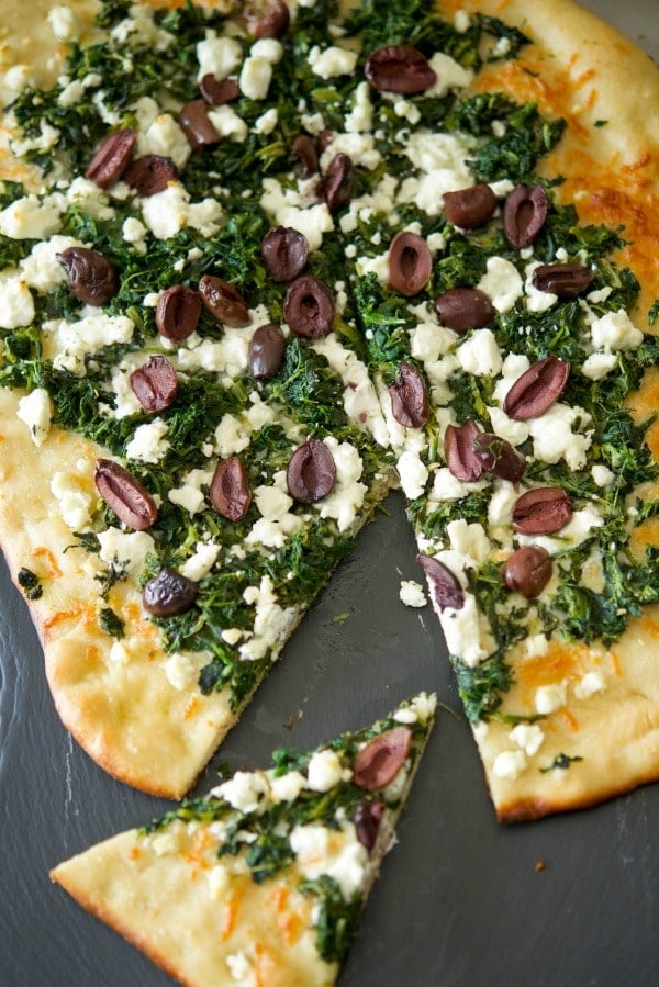 A pizza sitting on top of a wooden cutting board, Spinach, Goat Cheese, Olive Flatbread