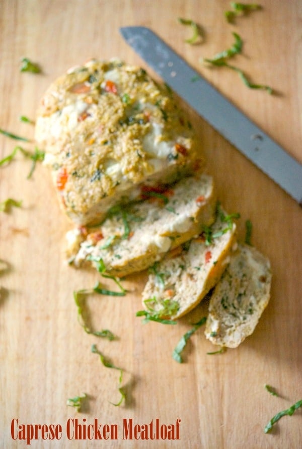 Caprese Chicken Meatloaf sliced on a wooden cutting board with a knife. 