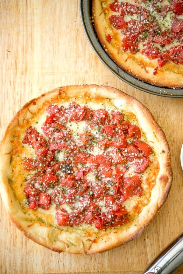 A deep dish pizza sitting on top of a wooden cutting board. 