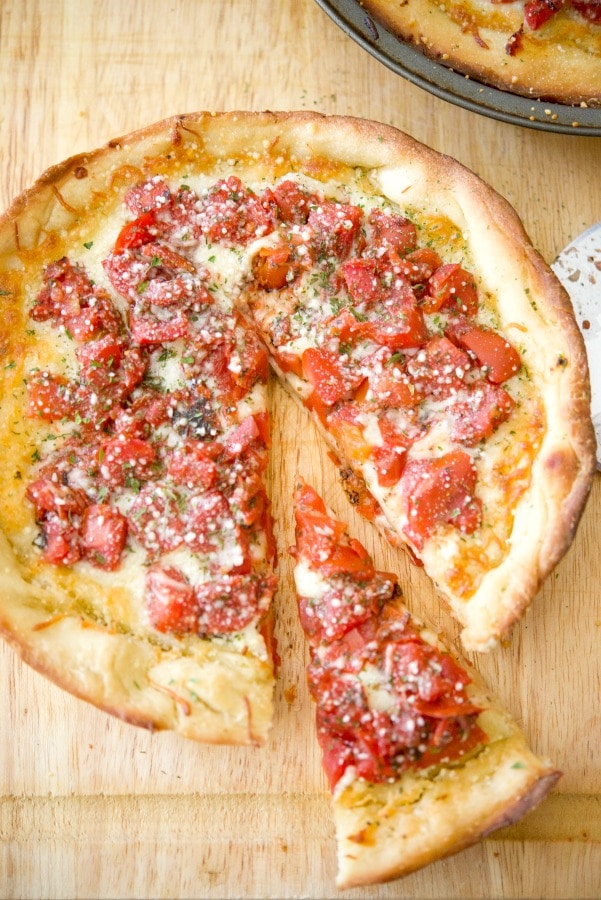 A slice of deep dish pizza sitting on top of a wooden cutting board