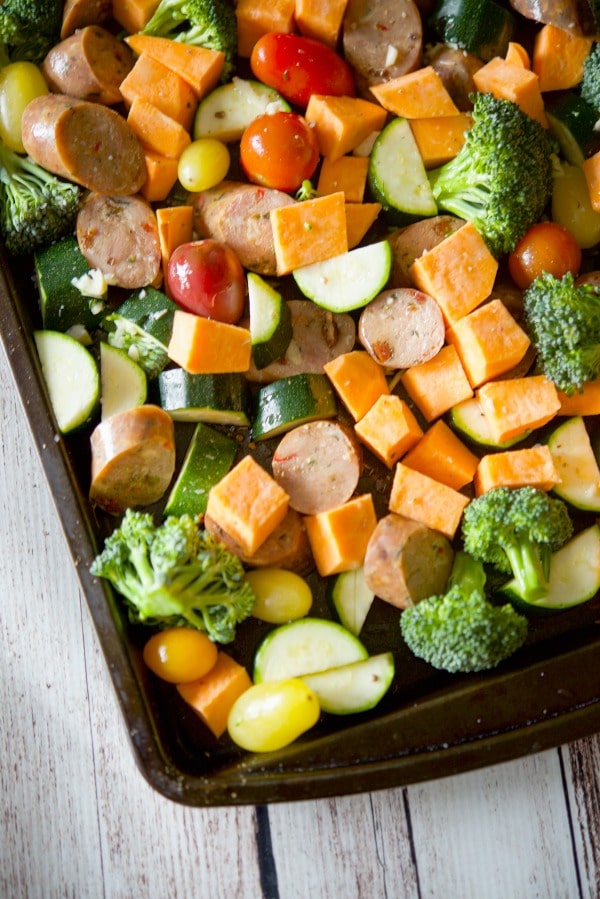 A close up of liced chicken sausage and vegetables on a sheet pan before cooked. 