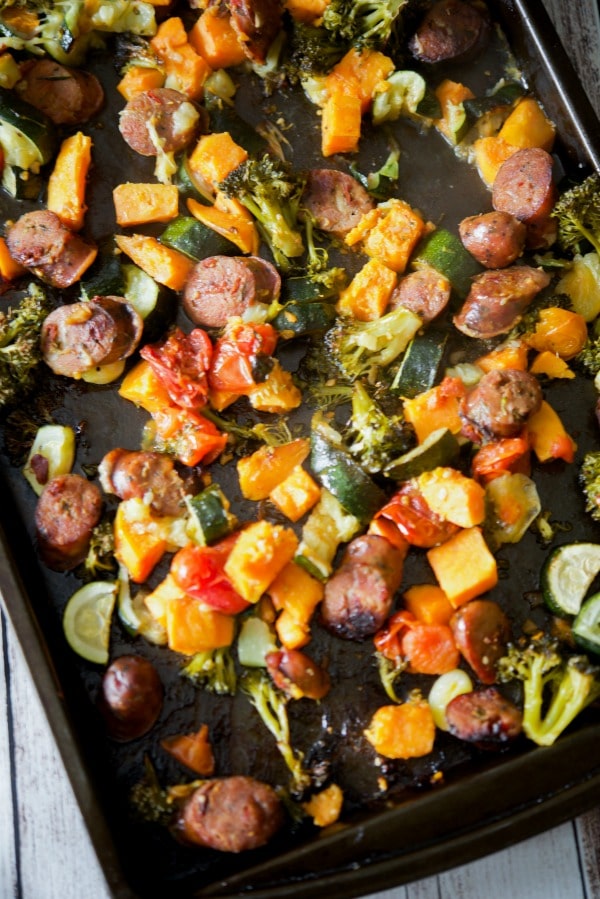 Cooked chicken sausage and vegetables on a sheet pan.