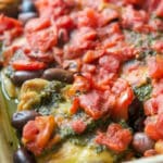 Pesto Chicken Thighs with fire roasted tomatoes and olives in a casserole dish