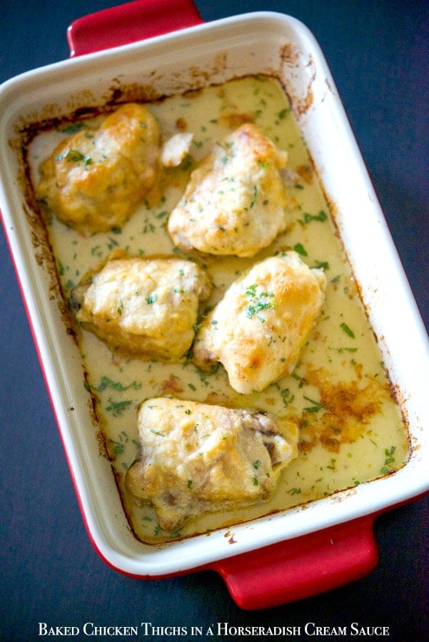 Chicken thighs topped with a horseradish cream sauce in a red baking dish. 