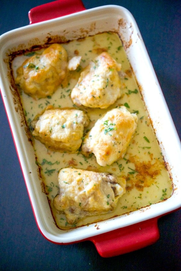 Bone-in chicken thighs topped with a horseradish cream sauce in a red baking dish. 
