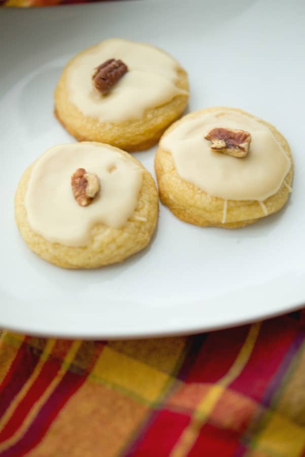 Maple Sugar Cookies coated with a maple syrup glaze and pecans on a white plate. 