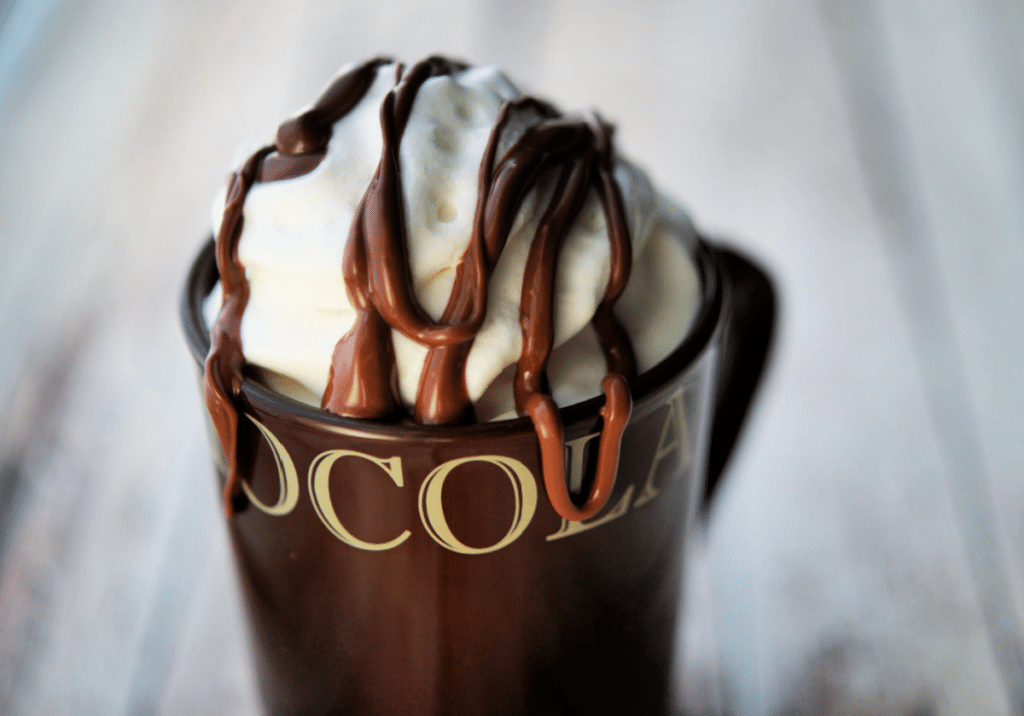 a close up of a brown mug with whipped cream and drizzled nutella