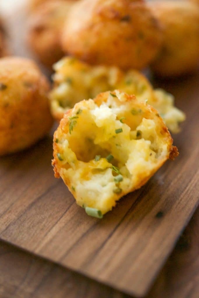 A close up of food on a wooden cutting board, with Potato puffs