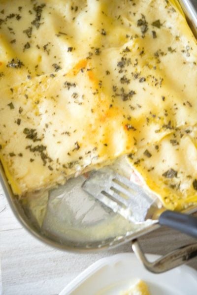 Chicken Saltimboca Lasagna in a metal pan with a piece cut out of it.