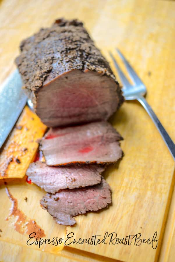 A piece of Espresso Encrusted Roast Beef on a cutting board with a knife and fork