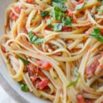 a close up of linguine with tomatoes and basil