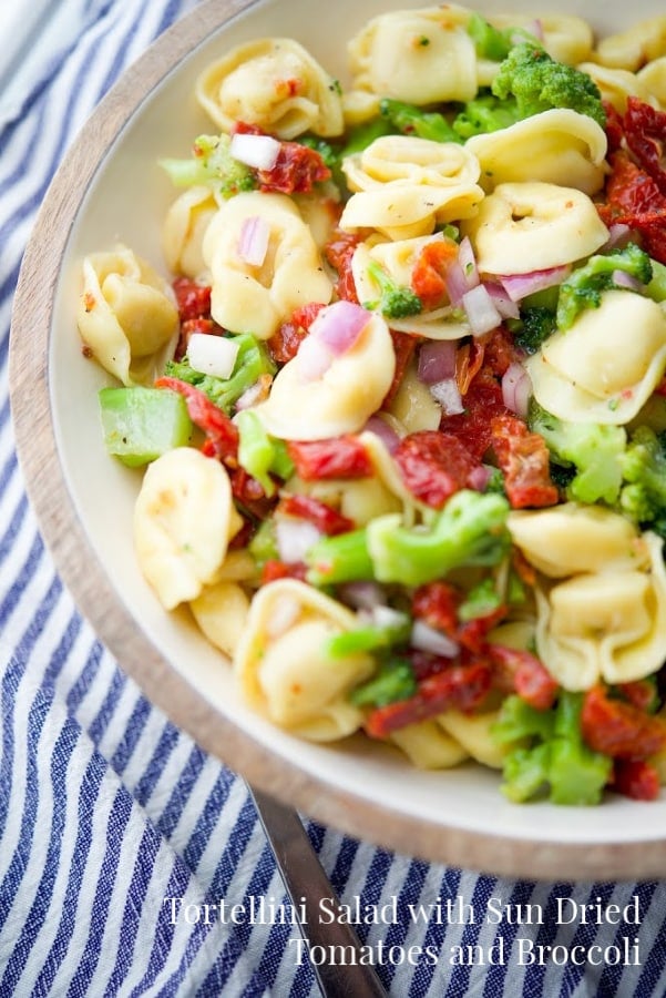 a bowl of cold tortellini salad with broccoli and sun dried tomatoes