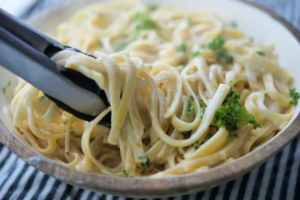 Fettuccine Alfredo in bowl with tongs