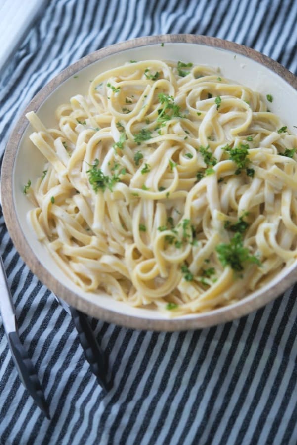 Fettuccine pasta tossed with a creamy alfredo sauce made with butter, garlic, cream and grated Pecorino Romano cheese in a bowl. 