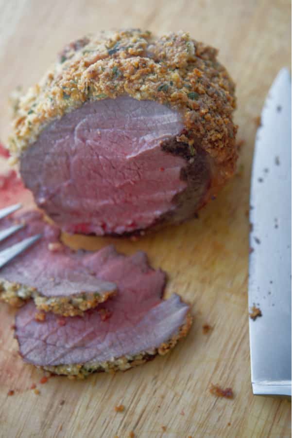 Top round roast beef encrusted with a mixture of Parmesan cheese, fresh parsley, garlic and panko breadcrumbs on a cutting board. 