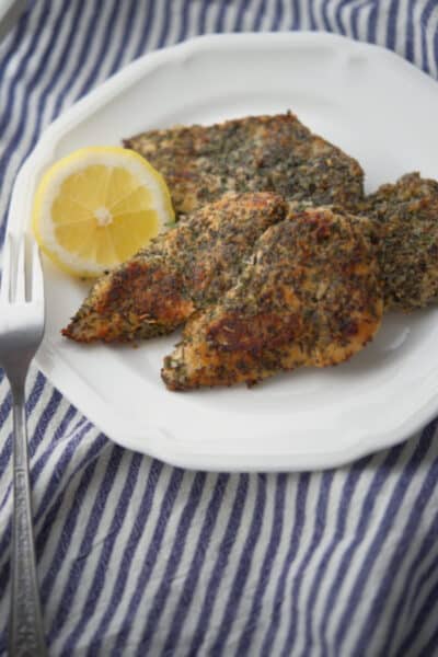 Boneless chicken breasts dredged in herbs and spices on a white plate.