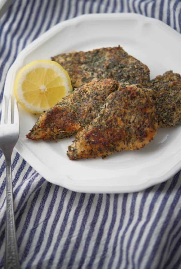 Boneless chicken breasts dredged in herbs and spices on a white plate. 