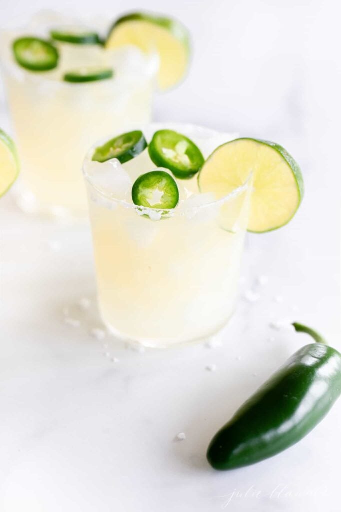 A close up of a spicy margarita in a glass with jalepeno garnish. 