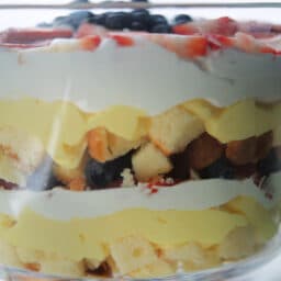 A close up of a berry trifle with yellow cake, berries, pudding and cream.