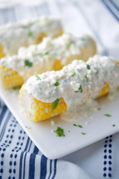 Grilled corn on the cob topped with a cajun lime crema on a white serving platter.