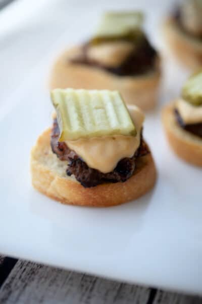 Cheeseburger Crostini with a pickle on a white plate