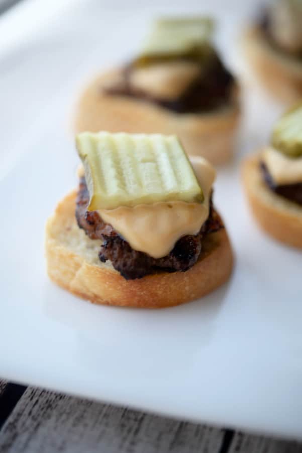 Cheeseburger Crostini with a pickle on a white plate