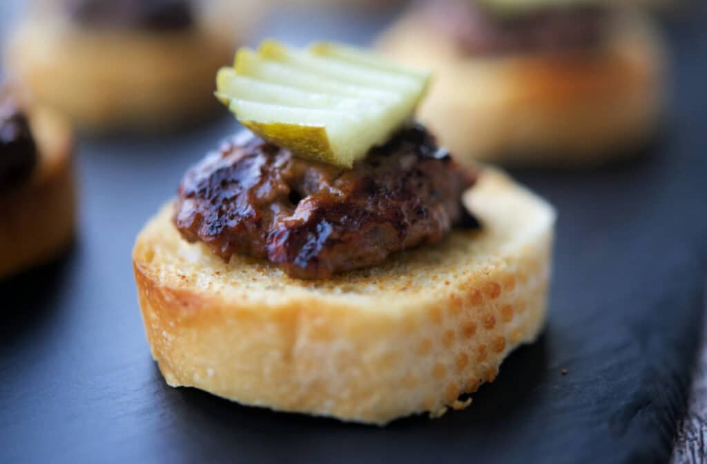 A close up of a cheeseburger on a crostini.