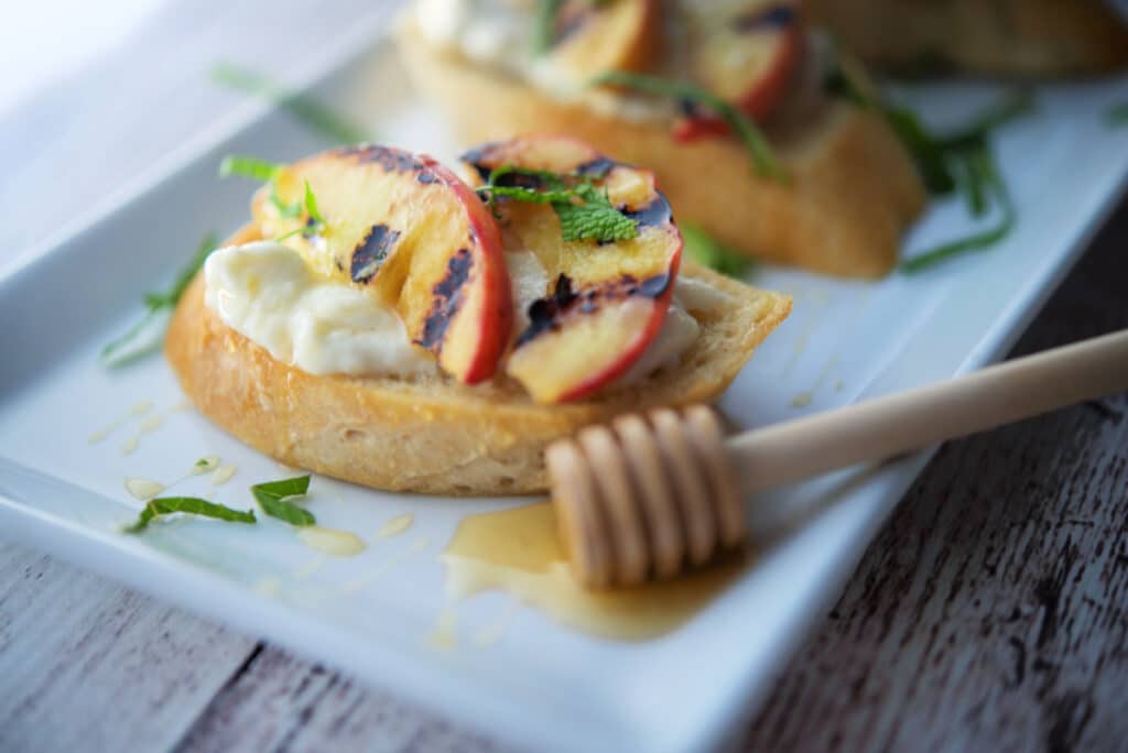 A close up of grilled peach crostini on a white platter