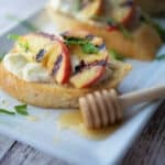 A close up of grilled peach crostini on a white platter