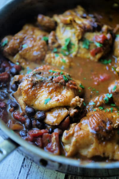 Chicken thighs in a skillet with black beans and tomatoes