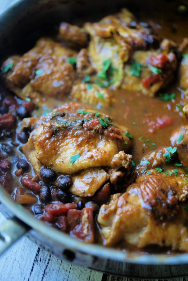 Chicken thighs in a skillet with black beans and tomatoes