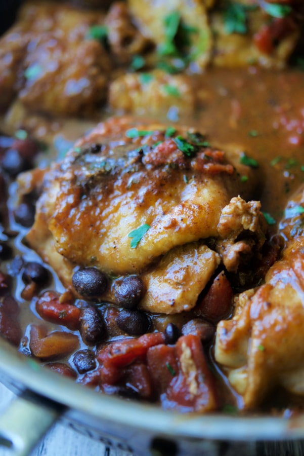 A chicken thigh cooked Mexican style with beans in a skillet