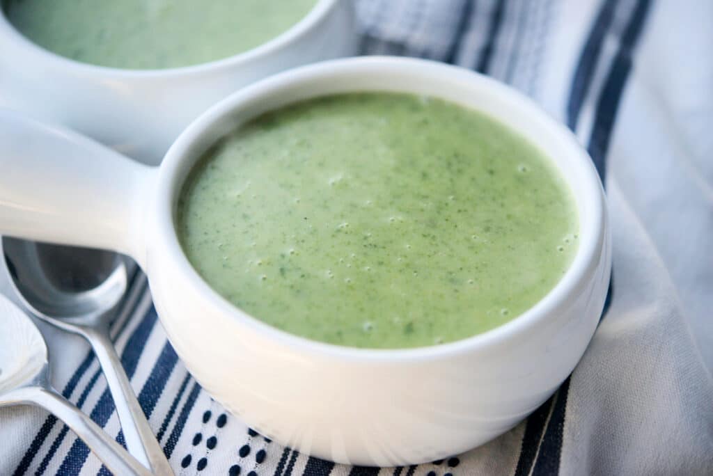 A close up of potato spinach soup in a white soup crock