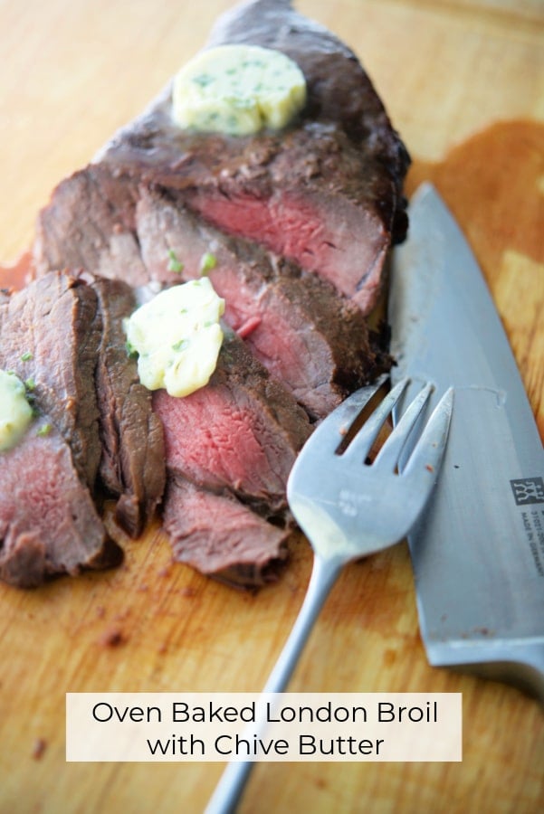 Cooked London broil on a wooden cutting board with chive butter. 