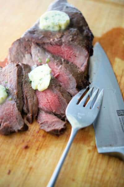 Cooked steak sliced on a wooden board with knife and fork
