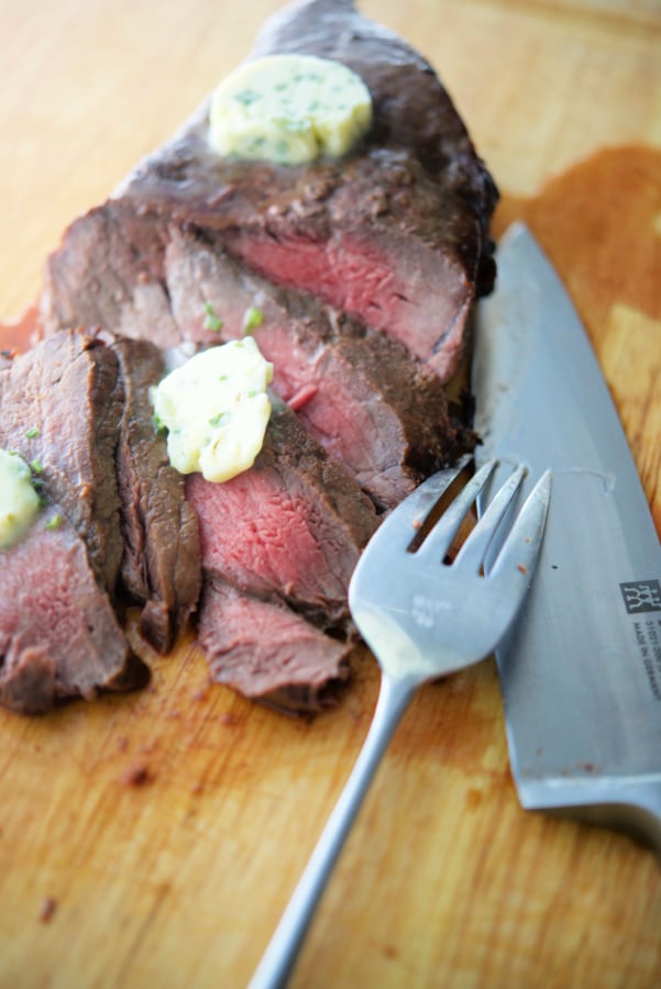 Cooked steak sliced on a wooden board with knife and fork