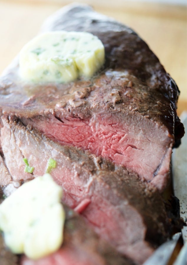 Sliced london broil on a cutting board with butter