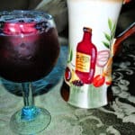 A close up of sangria in a glass on a table with a pitcher