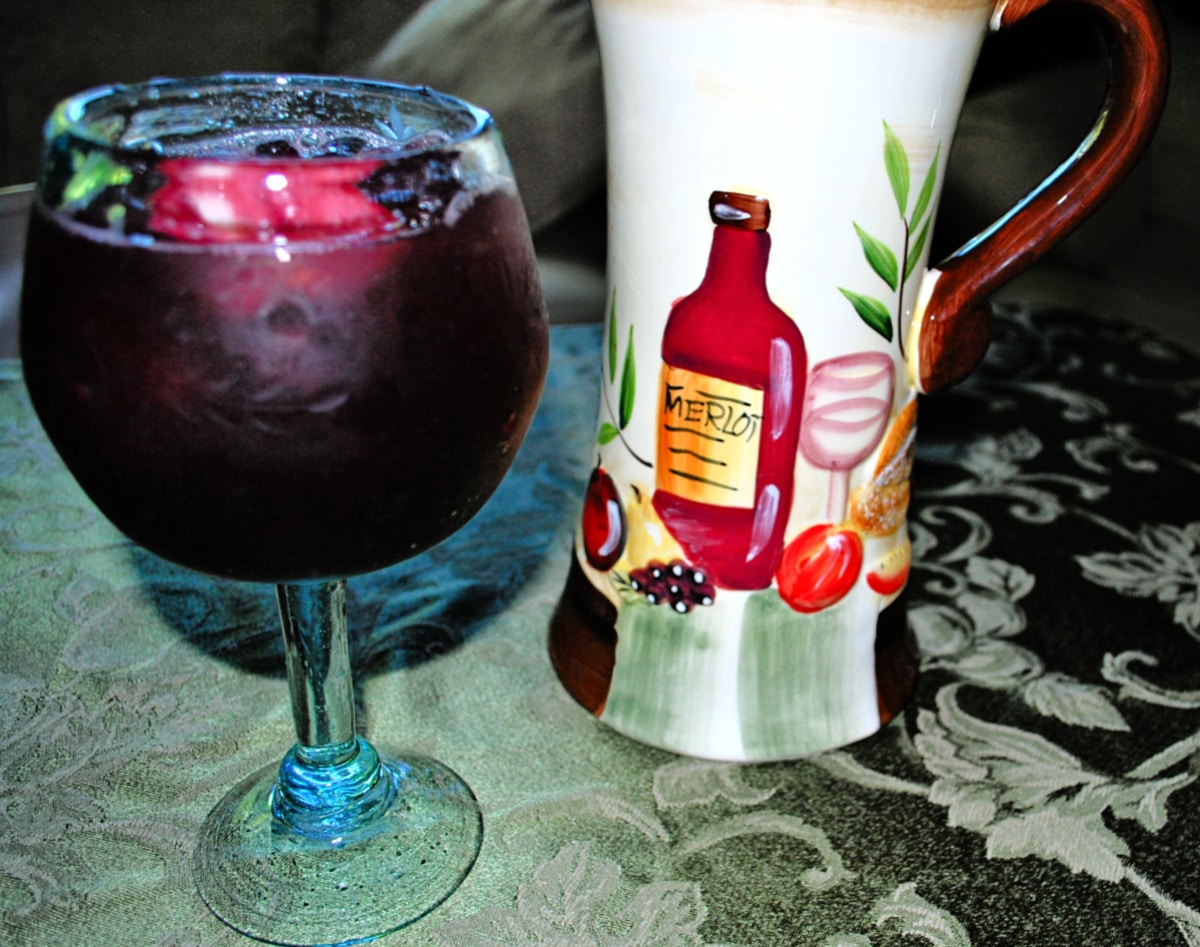 A close up of sangria in a glass on a table with a pitcher
