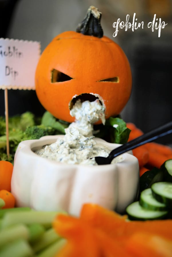 A carved pumpkin throwing up dip on vegetables