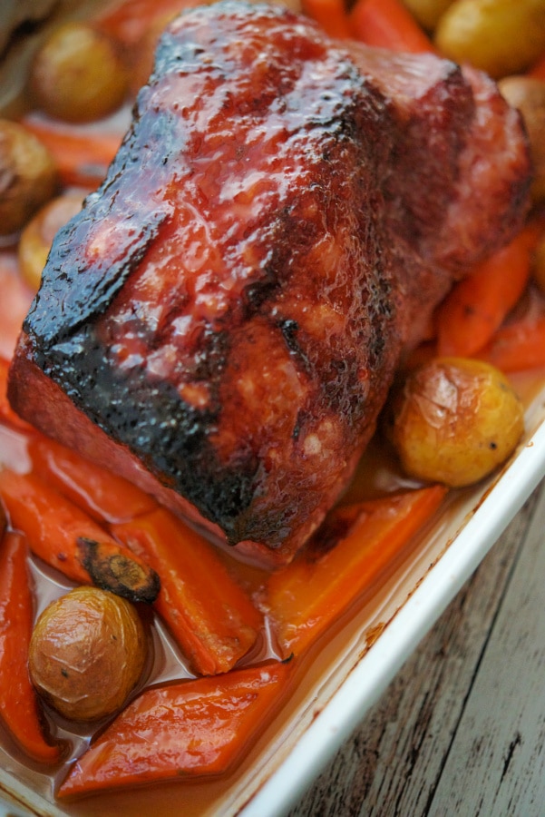 a whole corned beef in a baking dish with carrots and potatoes