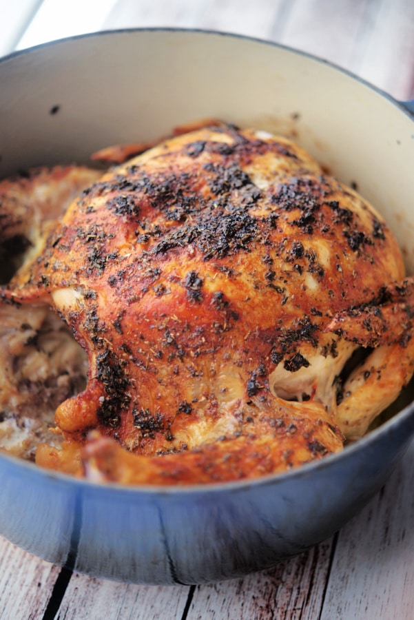 cooked whole roaster chicken in a blue Dutch oven