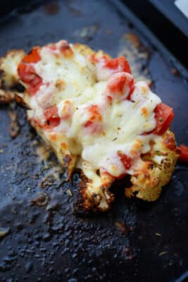 one cauliflower steak topped with tomatoes and cheese on a sheet pan